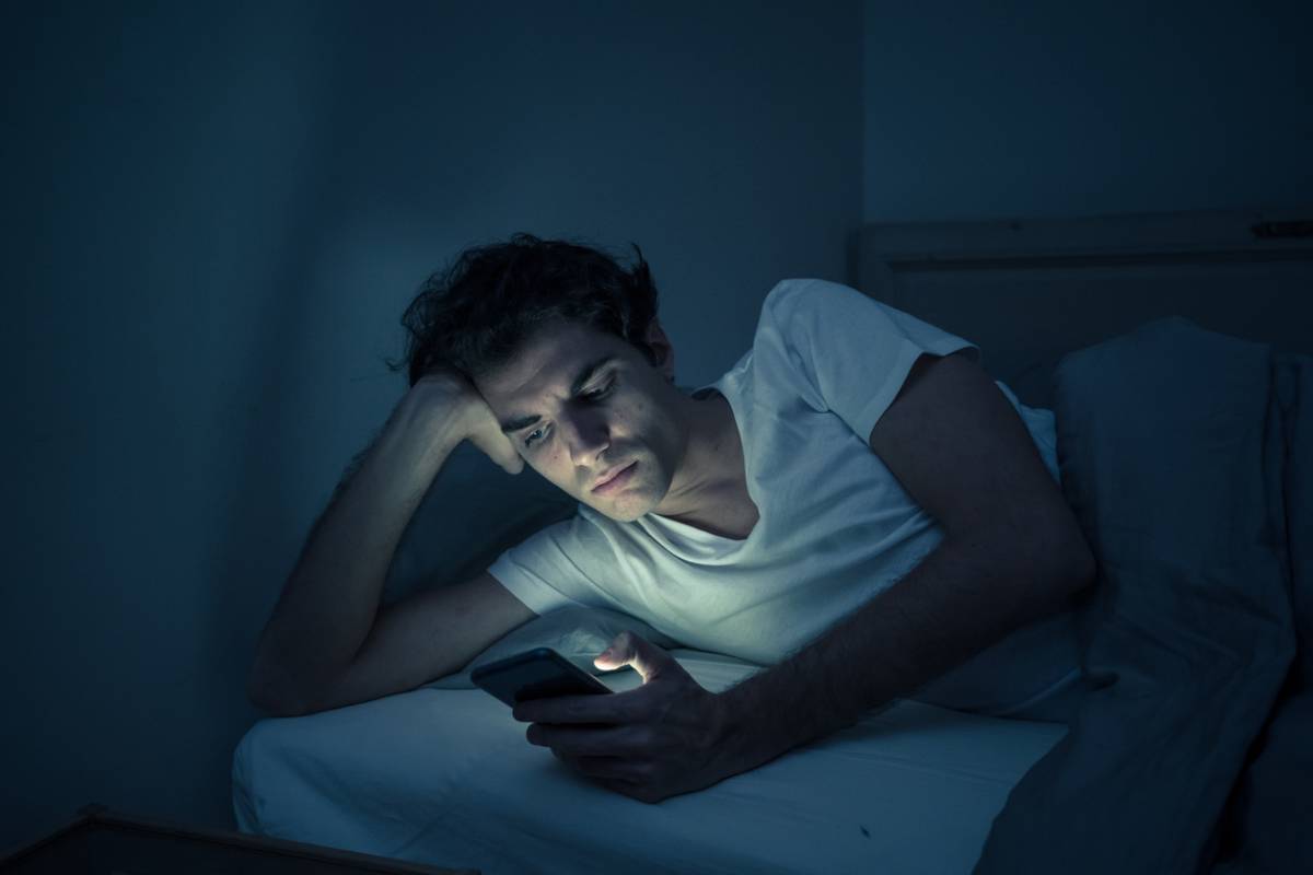 white man in bed looking at phone