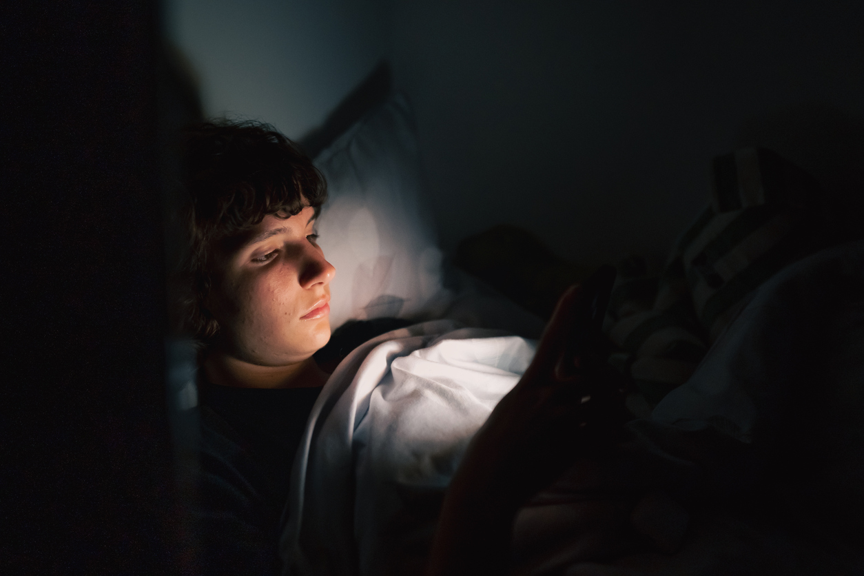 The image shows a teen in a dark room on their phone as the featured image for "At What Age Does Insomnia Develop?"