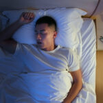 The image shows a man snoring at night to explain the age snoring will often begin.
