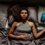 The image displays an African American woman lying in bed with trouble sleeping to show the most common sleep disorders.