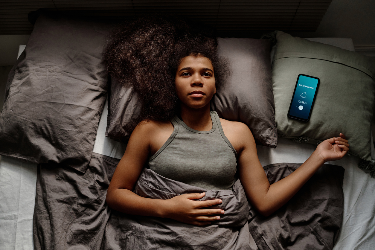 The image displays an African American woman lying in bed with trouble sleeping to show the most common sleep disorders.