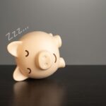 sleepy piggy bank on its side representing trying to make up sleep debt concept