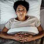Woman lying awake in bed with insomnia, showing difficulty sleeping and restlessness at night.