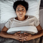 Woman lying awake in bed with insomnia, showing difficulty sleeping and restlessness at night.