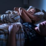 Woman covering ears with a pillow to block out partners snoring.