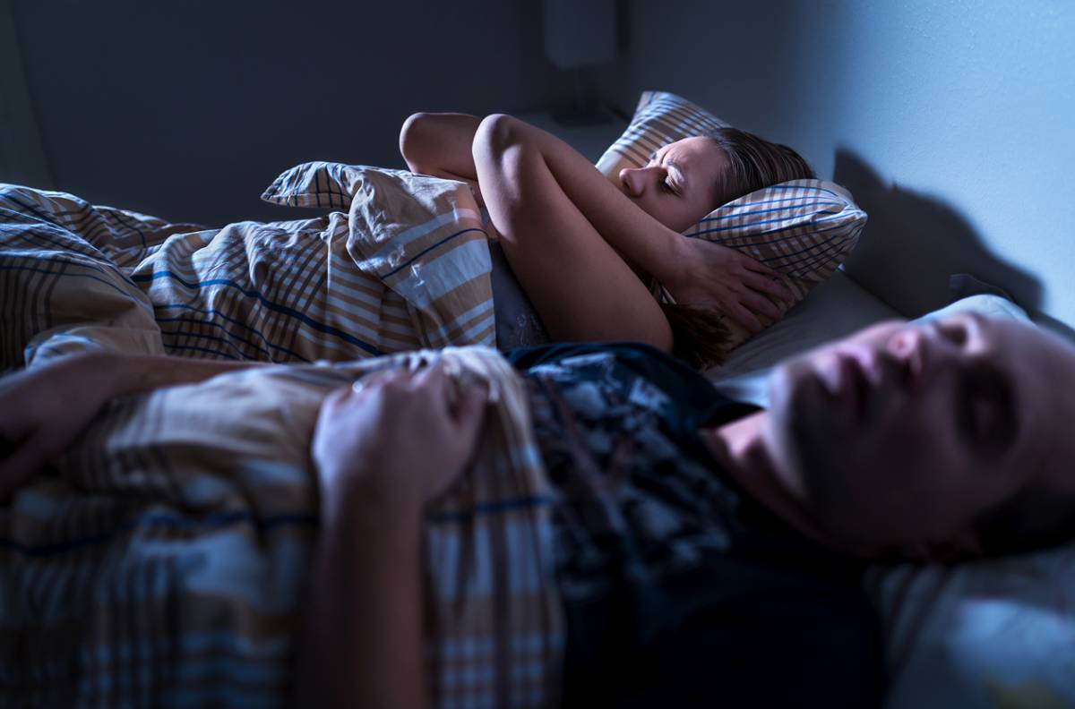 Woman covering ears with a pillow to block out partners snoring.