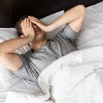 Man in bed, covering face due to restless sleep.