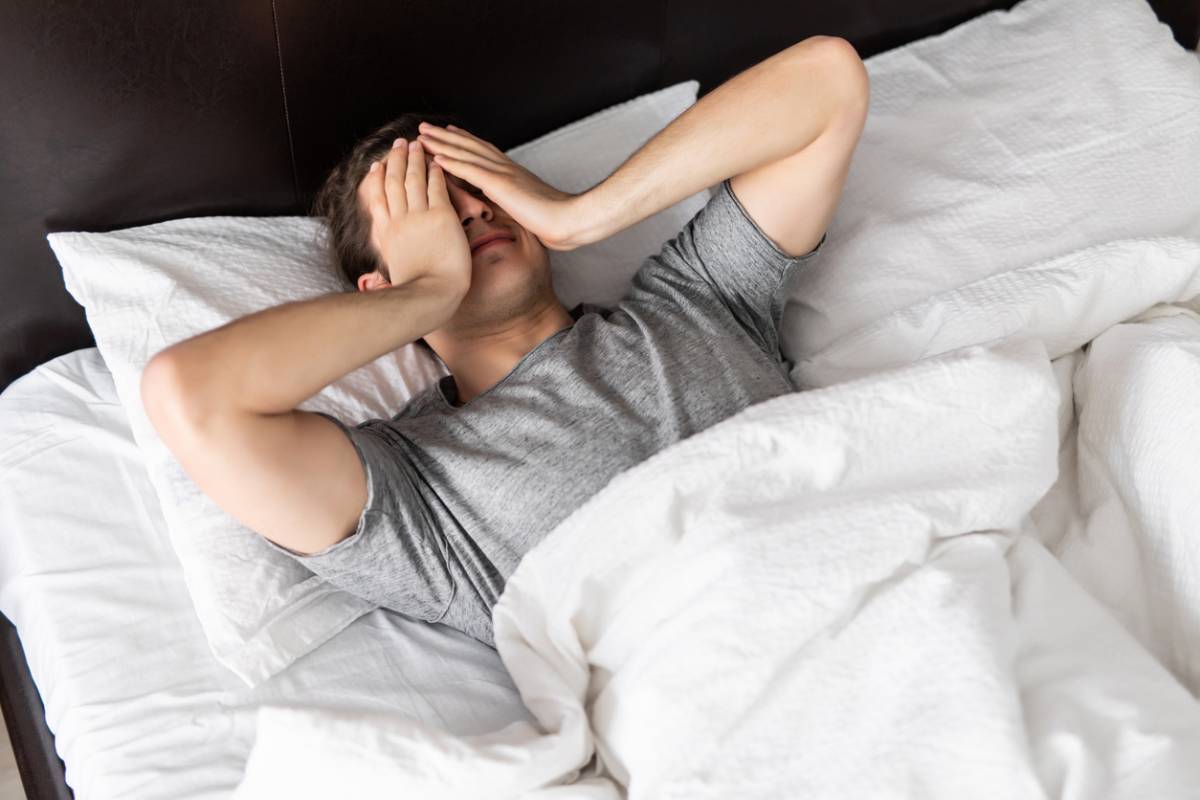 Man in bed, covering face due to restless sleep.