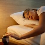 Tired woman turning of her alarm clock while sleeping in a bed.